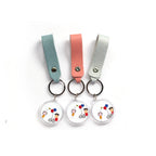 Three leather strap photo keychains with cartoon artwork on acrylic discs