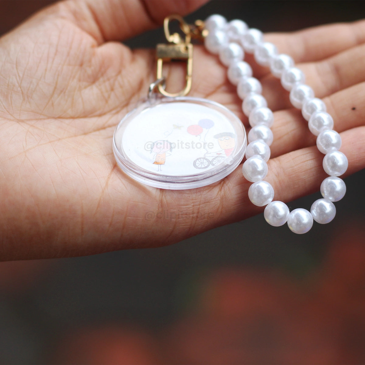 Pearl wristlet photo keychain with cartoon artwork, held up outdoors